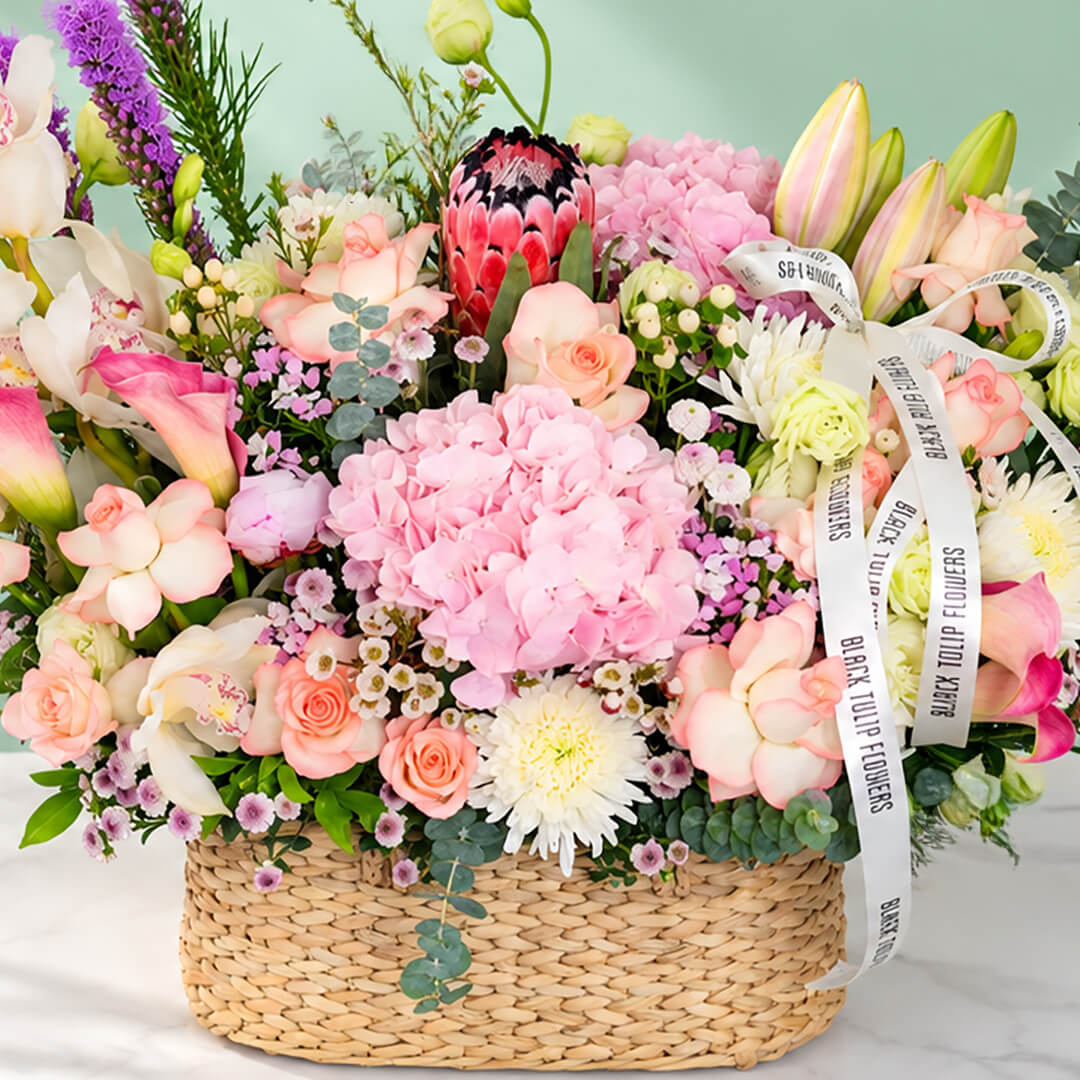 Assorted flowers including roses, hydrangea, calla lily, cymbidium, and Queen Protea arranged in a rectangular basket