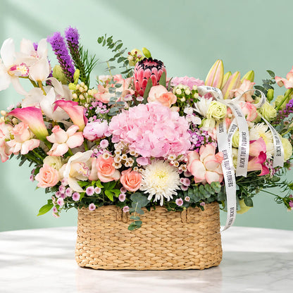 Assorted flowers including roses, hydrangea, calla lily, cymbidium, and Queen Protea arranged in a rectangular basket