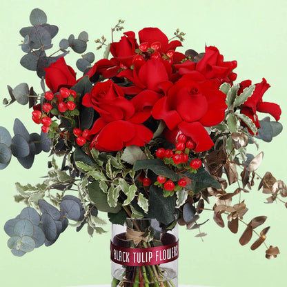 25 red roses with eucalyptus and berries arranged in a clear glass vase