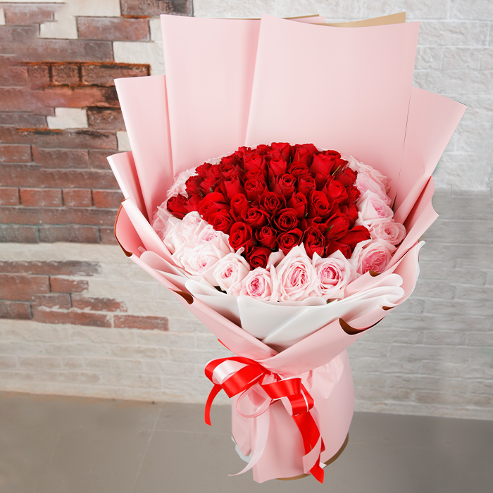 Heart-inspired bouquet of red and pink roses in soft pink wrapping
