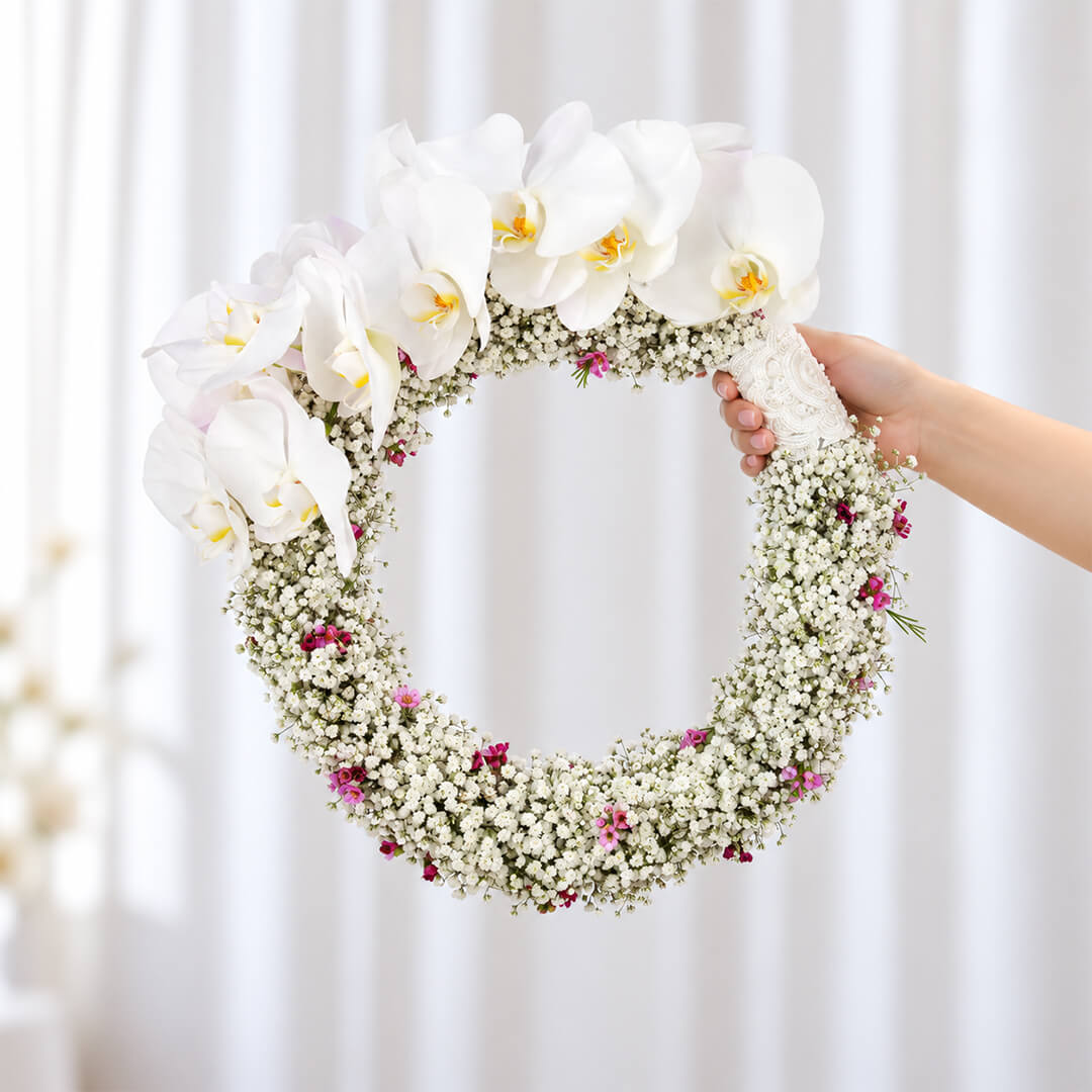 White Cymbidium bridal wreath with Gypsophila, wax flowers, and steel grass in a circular design