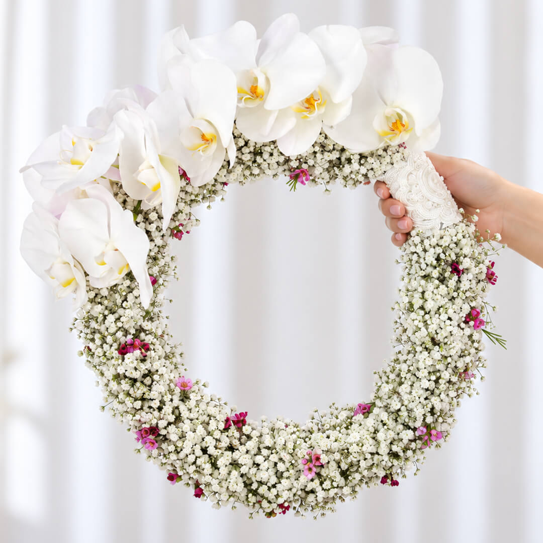 White Cymbidium bridal wreath with Gypsophila, wax flowers, and steel grass in a circular design