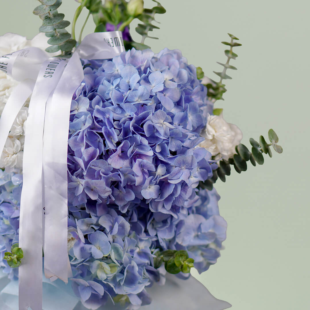 Blue hydrangea vase arrangement with fresh greenery and white ribbon accents