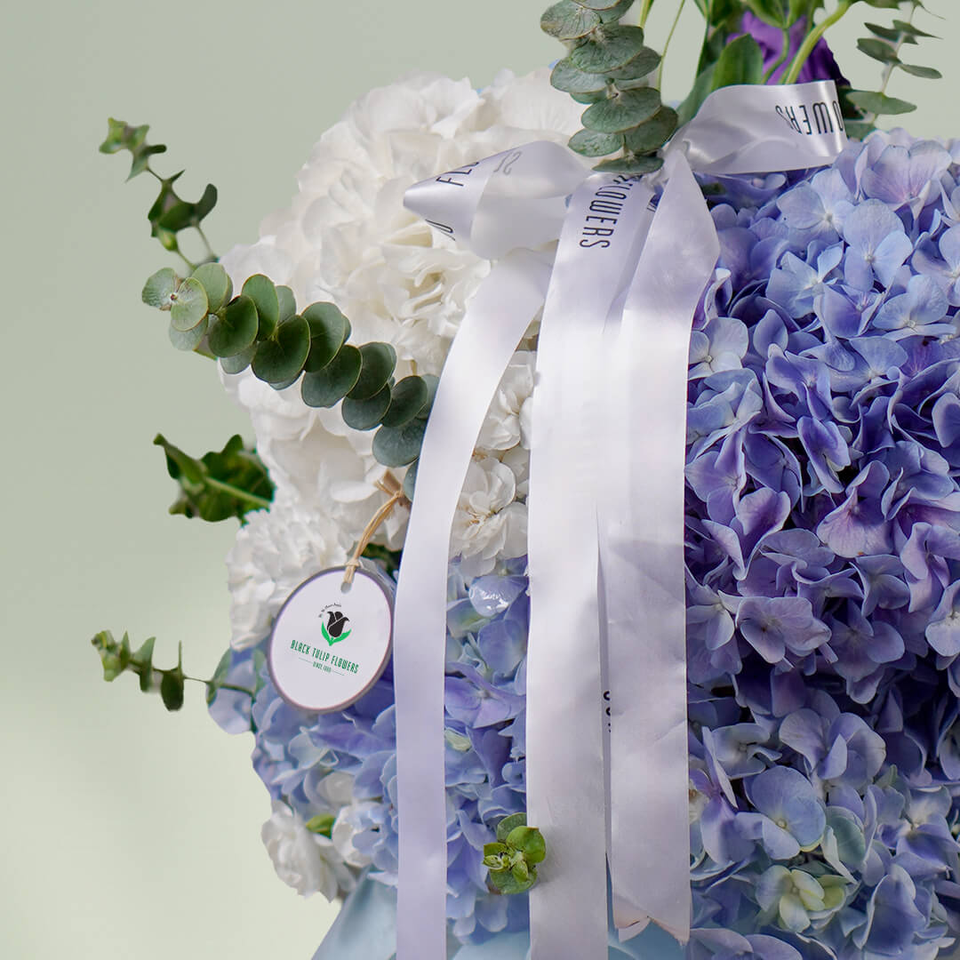 Blue hydrangea vase arrangement with fresh greenery and white ribbon accents