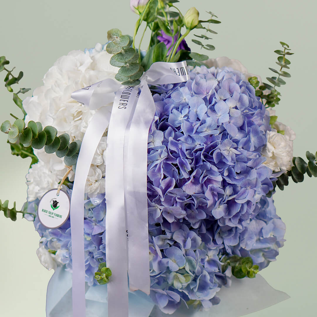 Blue hydrangea vase arrangement with fresh greenery and white ribbon accents