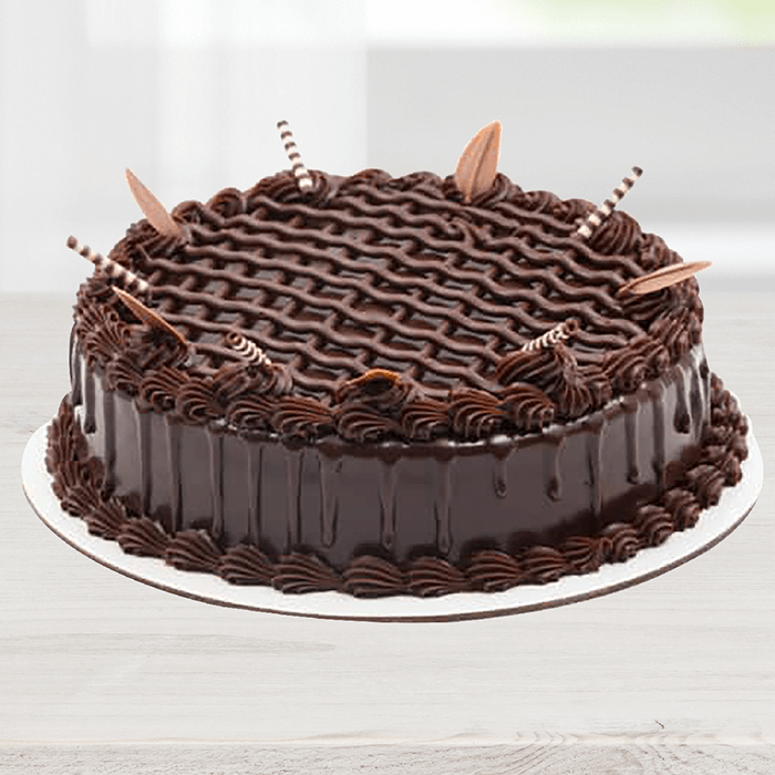 Triple Chocolate Cake featuring glossy chocolate frosting, piped swirls and decorative chocolate pieces.