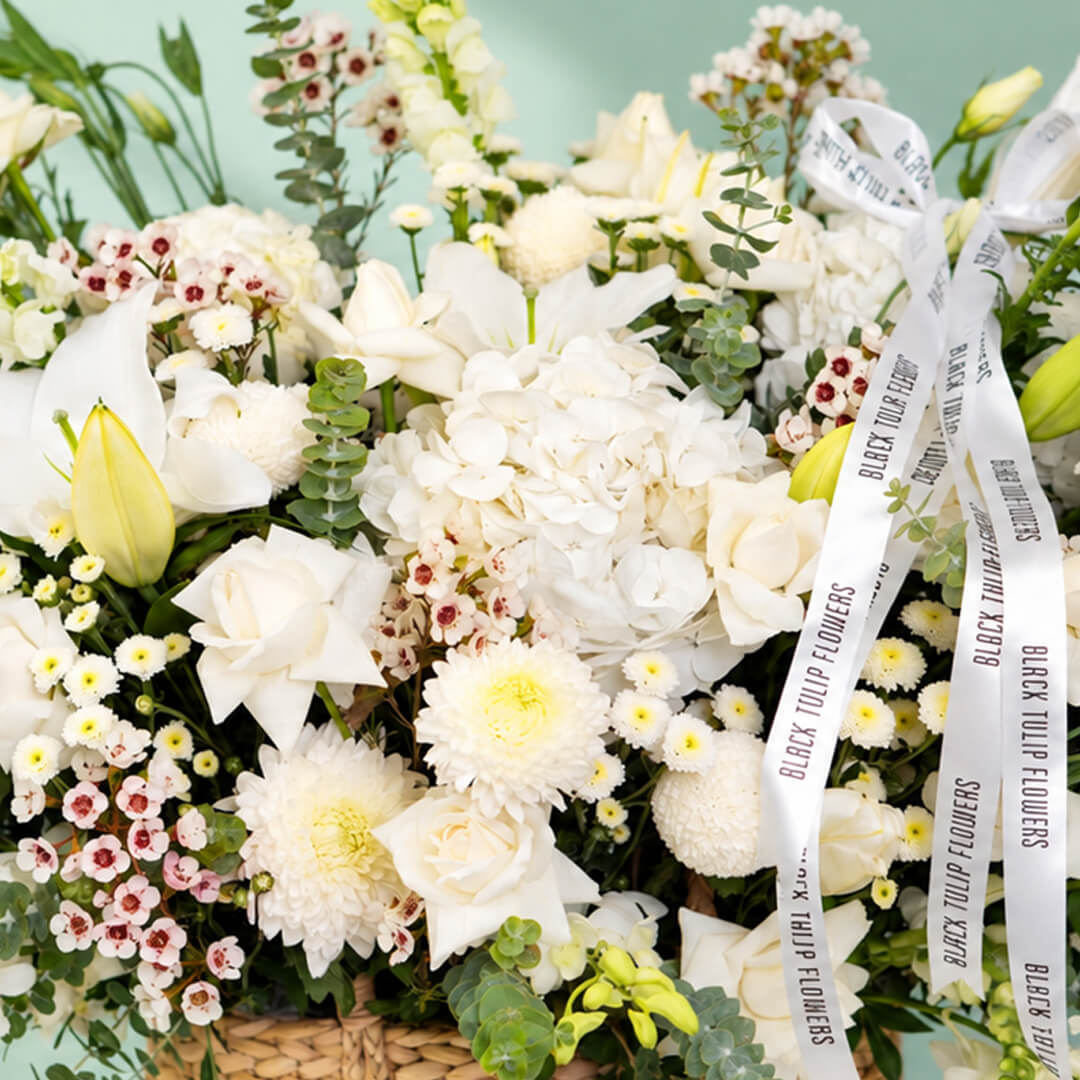 White flower basket featuring roses, hydrangea, lily and orchid with fresh greenery