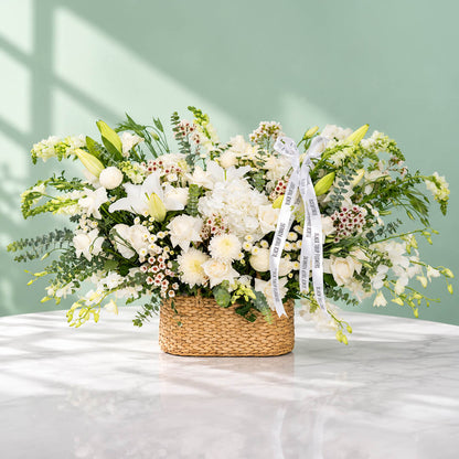 White flower basket featuring roses, hydrangea, lily and orchid with fresh greenery