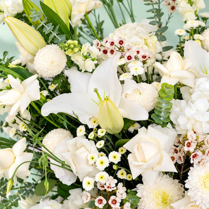 White flower basket featuring roses, hydrangea, lily and orchid with fresh greenery