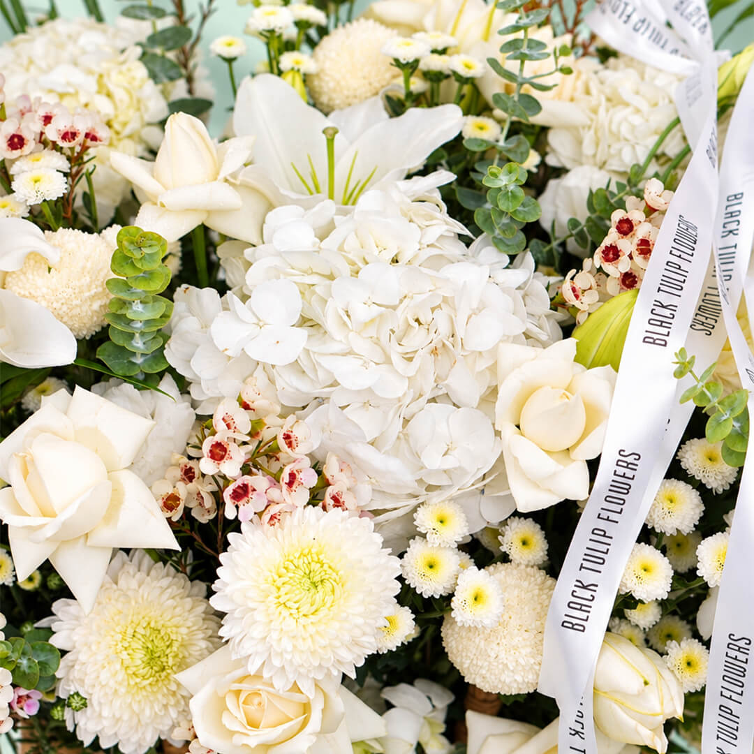 White flower basket featuring roses, hydrangea, lily and orchid with fresh greenery