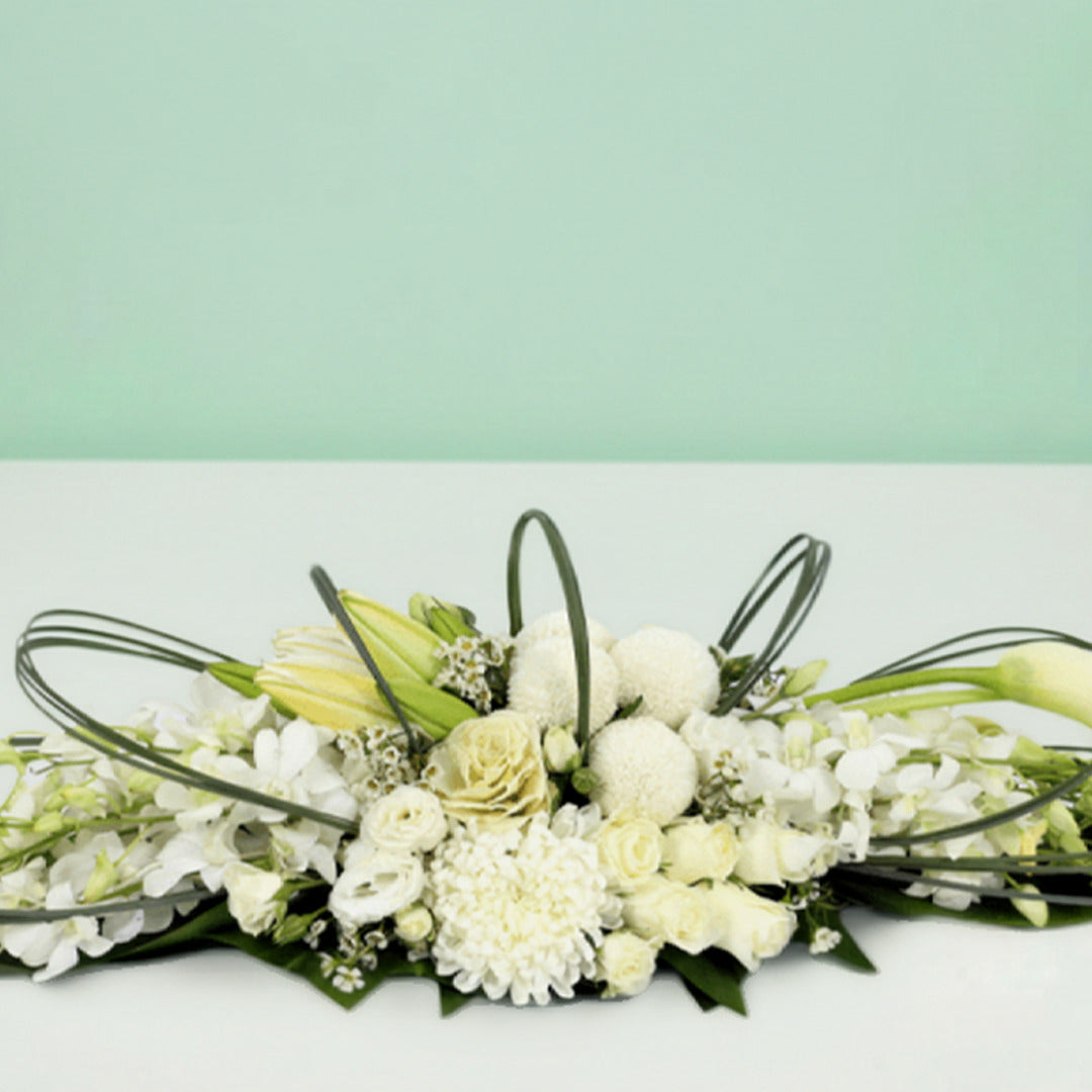 White long low flower arrangement with orchids lilies roses chrysanthemums and fresh greenery