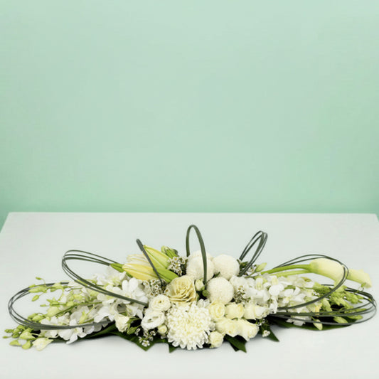 White long low flower arrangement with orchids lilies roses chrysanthemums and fresh greenery