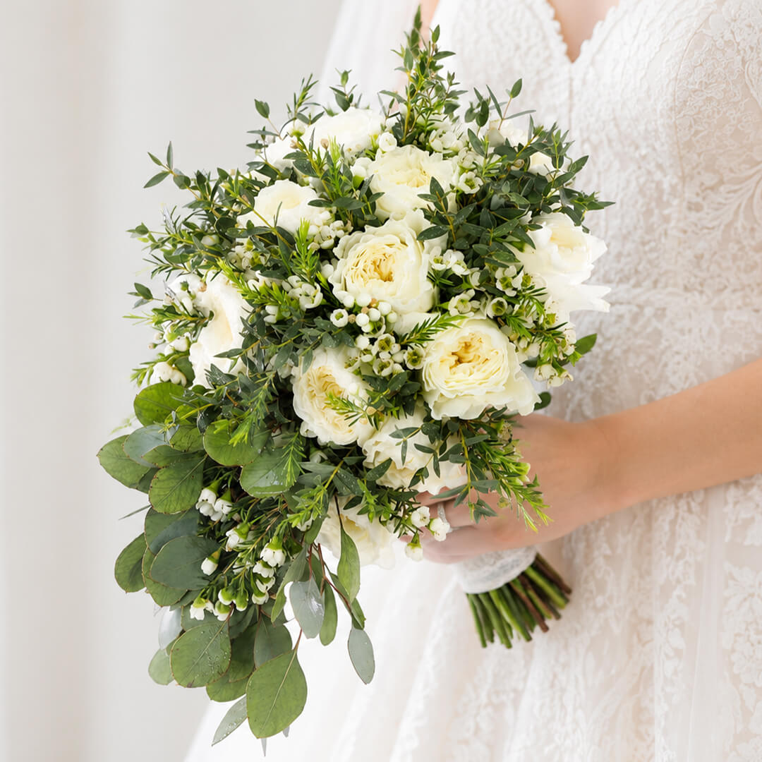 Premium white rose bouquet with a minimalist hand-tied design, accented with eucalyptus and wax flowers.