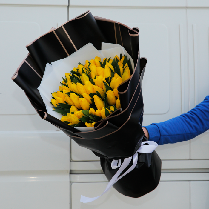 Yellow tulips arranged in layered black and white non-woven wrapping