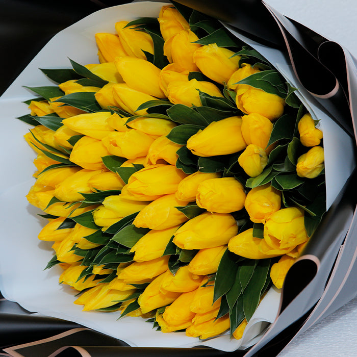 Yellow tulips arranged in layered black and white non-woven wrapping