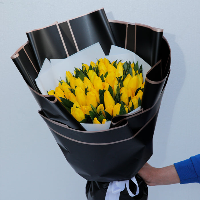 Yellow tulips arranged in layered black and white non-woven wrapping