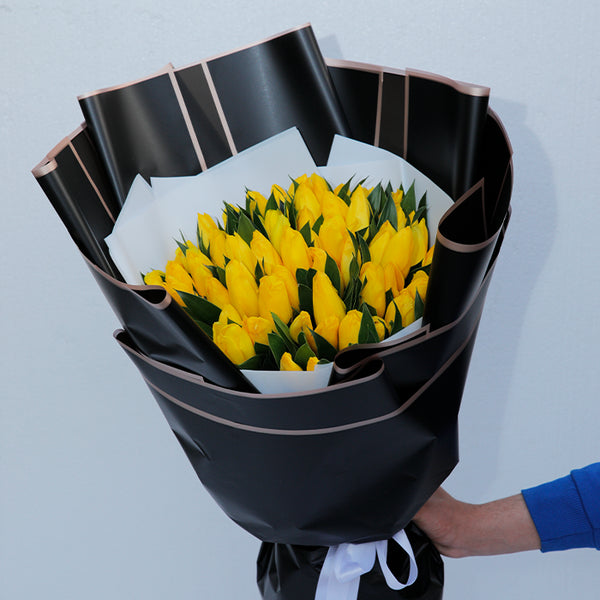 Yellow tulips arranged in layered black and white non-woven wrapping