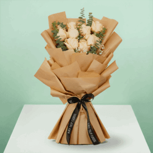 Peach roses artfully arranged with eucalyptus, wrapped in brown non-woven paper, and tied with a black satin ribbon.